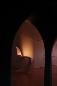 A dimly lit room with a white chair on a hardwood floor, creating a sense of depth and prominence in a modern space with clean lines and minimal decoration