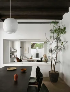 Open living area with a dining table, chairs, a potted plant, and a vase, surrounded by ample seating options and bright atmosphere