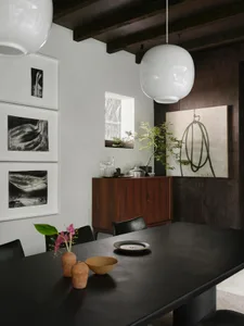Elegant dining space with a black table, three chairs, and a potted plant, featuring a vase with flowers as a centerpiece