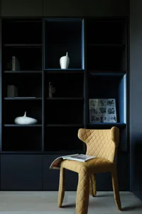A dark room with a black bookshelf filled with books and a chair, creating a cozy atmosphere perfect for reading and relaxation