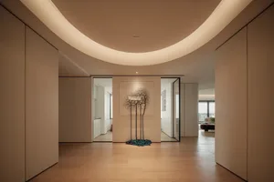 A modern living area with a large white wall featuring a painting of tree branches, wooden floors, and a chair, with a clean and minimalistic atmosphere