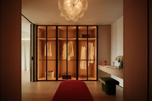 A well-lit bedroom with wooden floors, a red carpet, two wooden closets, a bed, and decorative vases