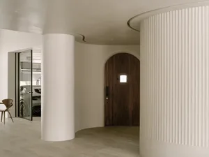 A curved hallway with two doors, one near the center and another towards the right, featuring wooden walls and a cozy atmosphere