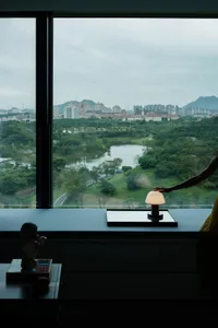 Cozy urban living area with a large window offering a panoramic city view, a couch, chair, and dining table, with a book on the table
