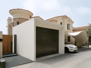 A modern house with a large archway leading to the garage area, featuring a white garage door and a black car parked in front, with two additional cars visible in the scene