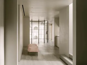 A white room with a pink bench and two chairs, featuring a large window for natural light