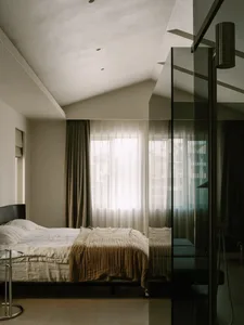 A calm bedroom with a white bed, two nightstands, and a chair, set against a window with a serene atmosphere