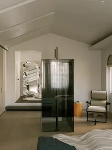 Elegant bedroom with a glass shower enclosure, wooden floors, and a white color scheme, featuring two chairs and a book on the floor