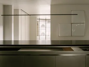 Empty kitchen with a stainless steel countertop island in a white-themed space with a bright and airy feel