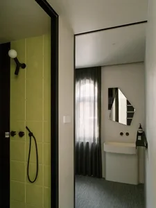 Bathroom with green and yellow walls, a white sink, a mirror, and a shower area, with a bottle on a surface