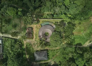 A serene photo of a circular building surrounded by trees in a forest, with a central gathering point and lush greenery