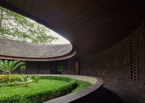 A serene architectural scene featuring a circular building with a wooden dome, surrounded by a lush green garden and potted plants, with two benches for seating