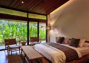 Cozy bedroom with two beds, a wooden floor, and natural light from windows, featuring striped and plain bedding, and two chairs