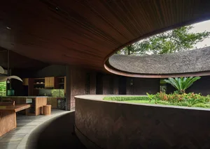 Open living area with wooden floors and walls, potted plants, and a refrigerator in the background, featuring a modern and spacious design with natural elements
