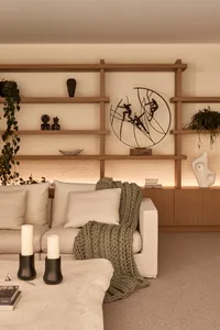 Cozy living room with wooden floors and walls, featuring a dining table, multiple chairs, and couches, with books and potted plants adding to the warm ambiance