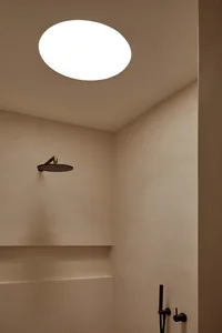 A modern bathroom with a concrete finish, featuring a metal shower head mounted on the wall, creating an industrial touch