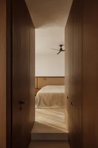 A bedroom with a neatly made bed, wooden doors, and a fan, creating a cozy atmosphere