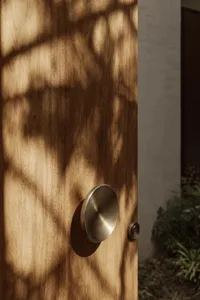 A modern interior doorway with a wooden door and a silver handle, surrounded by a bright and inviting atmosphere with sunlight coming through the window