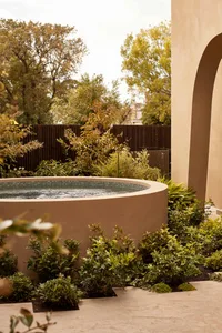 A serene outdoor patio area with a circular pool surrounded by lush greenery and potted plants, featuring water flowing over the pool's edge