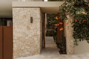 A serene entrance to a house with a brick wall, a doorway, and potted plants, set against a neutral background