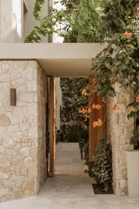 A welcoming outdoor patio area with a stone wall, wooden door, and potted plants, featuring benches for seating and a lively atmosphere