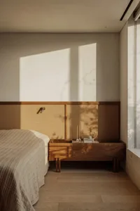 A calm bedroom with a large bed, two nightstands, and a vase, lit by natural sunlight through the window