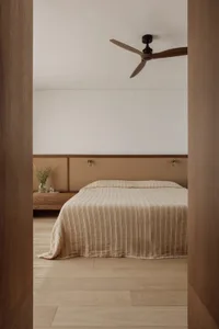 Cozy bedroom with a striped blanket on a hardwood floor, white walls, and a wooden headboard, with two potted plants and a vase nearby