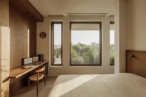 Bright and inviting bedroom with a wooden floor, a chair near the window, clocks, and a book on a surface