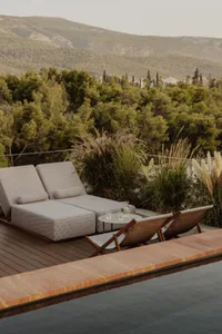 A well-lit outdoor patio area with lounge chairs and couches on a wooden deck near a pool, perfect for relaxation
