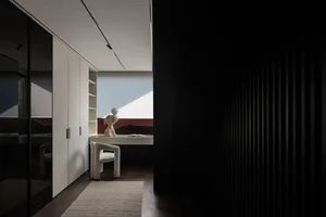 A minimalist room with a white plastic chair in front of a window, two books on the chair, and a black doorway to another area