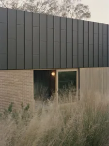 Exterior view of a house with a black roof, brick wall, and natural light from windows