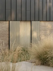 A brick building with a black roof, featuring two doors, one open and one closed, with natural light illuminating the scene