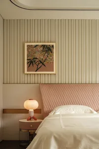 A cozy bedroom with a large bed, white bedding, and a painting of flowers on the wall, lit by two lamps and a vase