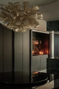 A sophisticated bar area with a large chandelier, dark countertops, and bottles on the counter