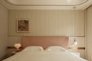 A cozy bedroom with a striped wall, a large bed, two lamps, and a painting above the bed
