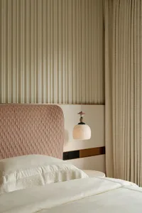 Cozy bedroom with a large bed featuring a pink headboard and striped design, two lamps, and a chair, creating a relaxing atmosphere