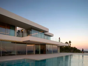 A modern white house with glass walls overlooking a swimming pool, featuring a spacious open concept living area with a calm and serene atmosphere