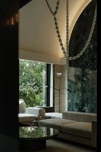 A modern living space with white couches and chairs in front of a large window, flooded with natural light and featuring marble accents