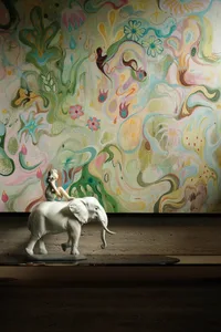 An elephant figurine sits on a table in front of a painting of a woman riding an elephant, set in a creative and imaginative environment