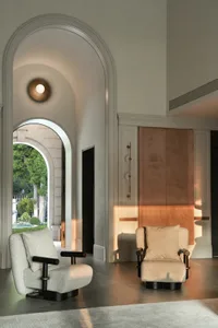 A well-lit living room with a white color scheme, two chairs in front of a doorway, and no people present
