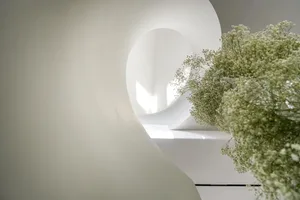 A calm indoor space with a white wall, a large vase with purple flowers, and a serene atmosphere