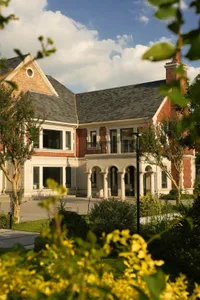 A traditional house with a brick exterior, a balcony, and multiple windows, set against a backdrop of trees
