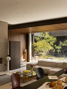 Modern living room with a couch, chair, dining table, and natural light from a large window, surrounded by books and clean lines