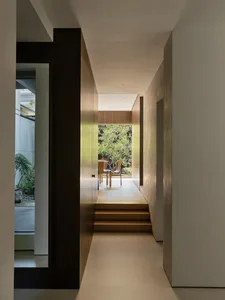 Wooden hallway with two doors, a dining table, and chairs, featuring a potted plant and warm lighting