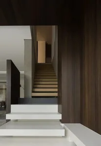 A clean and minimalist interior staircase with wooden steps and a brown color, leading to another level of the building