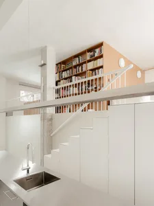 Open living area with a kitchen, wooden stairs, white cabinets, and scattered books creating a warm and inviting atmosphere
