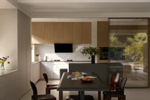 Open modern kitchen and dining space with wooden cabinets, glass dining table, and a potted plant, featuring a contemporary atmosphere