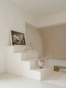 Clean and minimalist interior space with a staircase, artwork, and a vase, featuring white walls and a neutral color palette
