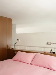 Cozy bedroom with a wooden platform bed, pink pillows, and two lamps, a clock on the wall, and a warm atmosphere