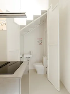A minimalist bathroom with two sinks, a toilet, and white tiles on the walls and floors
